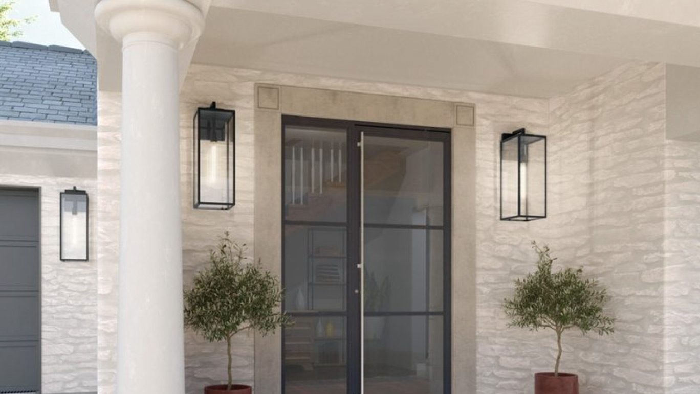 A modern entrance with glass double doors framed by two tall black Kichler lantern-style lights and two potted plants on either side, set against a light stone wall. It's the perfect backdrop for your latest social media post, with a white column standing gracefully on the left.