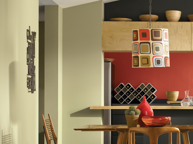 Modern kitchen with a geometric light fixture, red accent wall coated in Sherwin-Williams paint, and wooden bar counter. Decor includes bowls, a cactus plant, and abstract wall art.