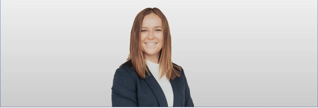 Tara Byrne, with straight, shoulder-length hair, wears a dark blazer and white top against a plain background, smiling at the camera as she joins Falls Expands Communications Team.