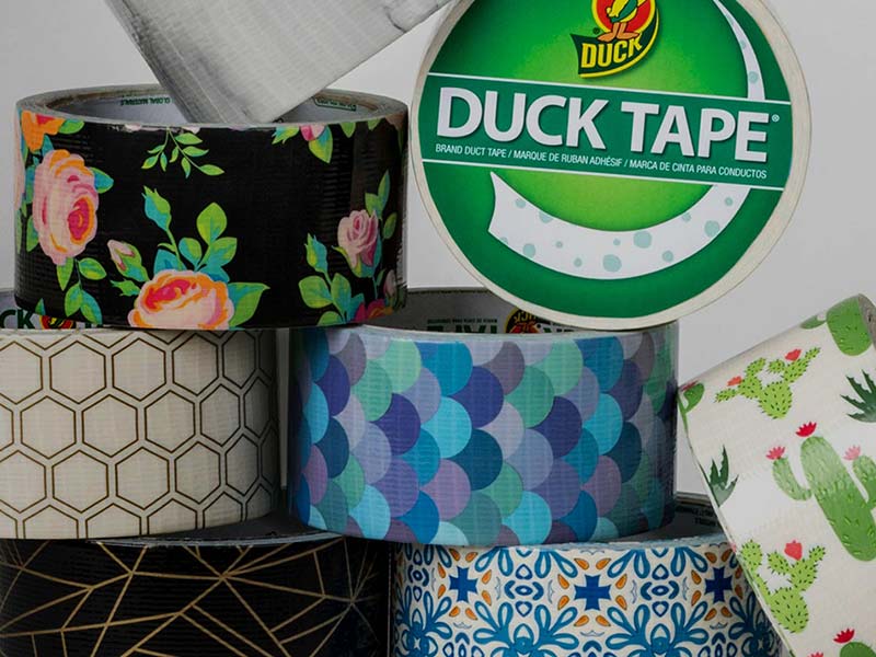 A collection of various decorative duct tapes, including floral, geometric, and cactus patterns. The tapes are stacked with a Duck Tape brand roll prominently displayed, showcasing the quality and creativity synonymous with the Brand.