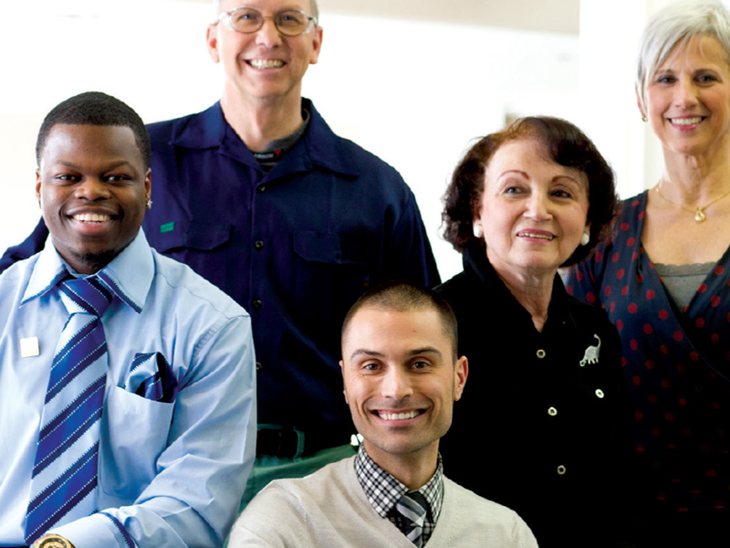 A group of five people, dressed in business and casual attire, smiling at the camera outside MetroHealth.