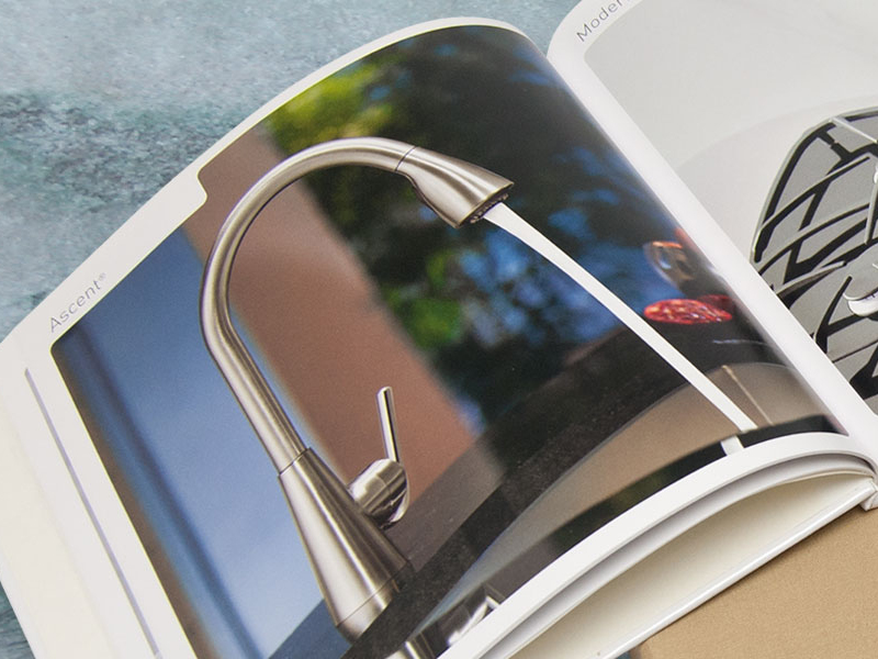 Open magazine displaying a photo of a Moen stainless steel kitchen faucet with water flowing from the spout, ideal for B2B showcases.