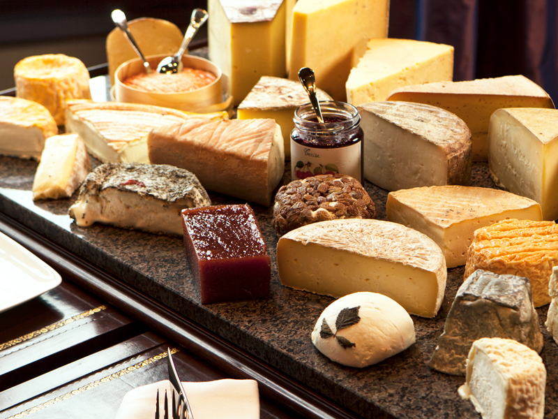 An assortment of various cheeses and condiments displayed on a slate serving board, with a jar of preserves from Edwins and utensils for serving.