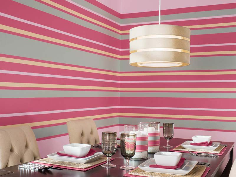 A dining room with pink, gray, and beige horizontal striped walls, meticulously created using painters tape. The table is set with plates, bowls, glasses, and candles. A large, modern pendant light hangs above the table.