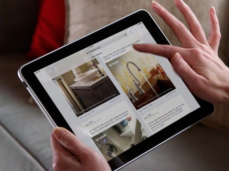 A person holding a tablet and scrolling through an app displaying home improvement images, including a MOEN sink and faucet.