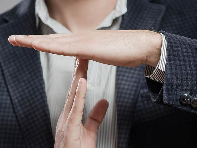 A person in a suit jacket making a "time-out" gesture with their hands, signaling the need to avoid saying the wrong thing on social media.