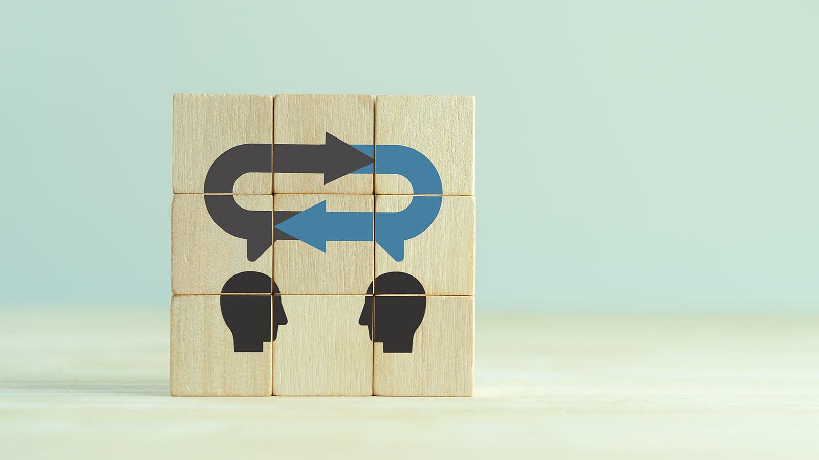 Wooden blocks showing two silhouettes of heads with a pair of arrows, one black and one blue, pointing between them, indicate the momentum of employee communications.