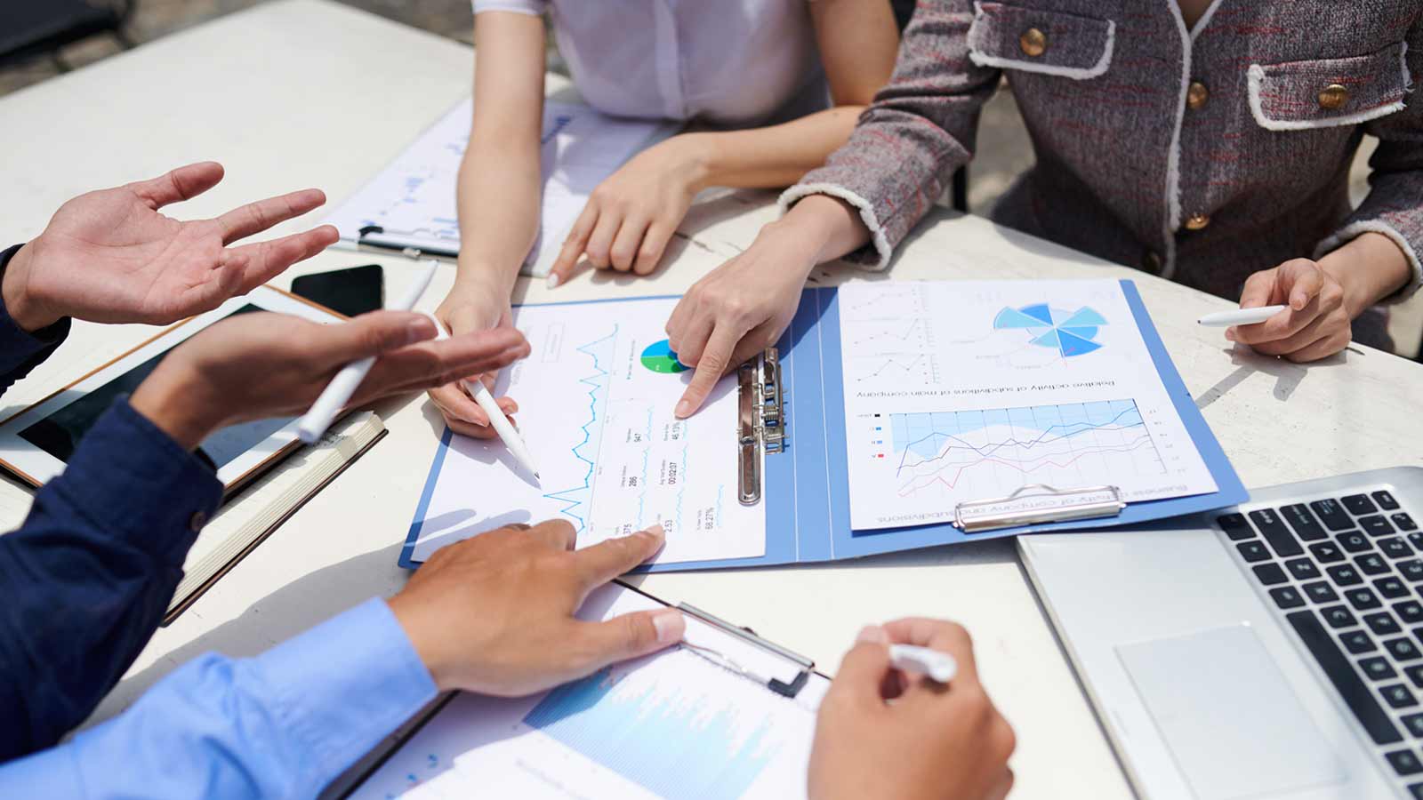 Four people are sitting around a table, reviewing and discussing graphs and charts on paper and a laptop, considering internal considerations for an effective brand strategy.