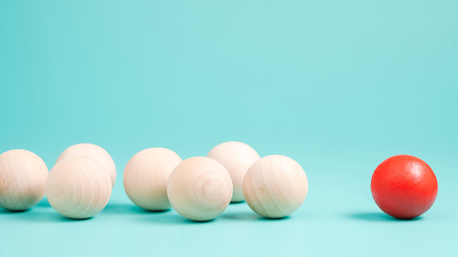 Several beige wooden balls are aligned on a blue background, with one red ball positioned slightly apart to the right, symbolizing an effective brand strategy standing out amidst external considerations.