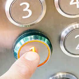 A finger presses the illuminated number one button on an elevator panel, nailing the elevator pitch by making a clear and confident start.