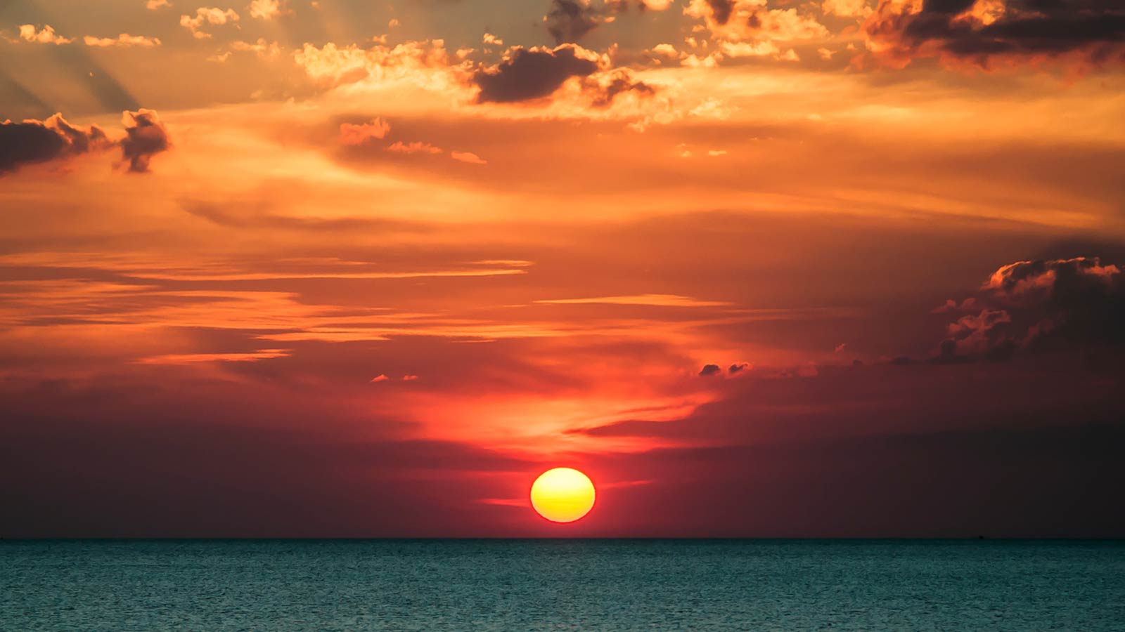 A vibrant sunset over a calm ocean with the sun partially below the horizon, and clouds scattered throughout the colorful sky evokes a sense of tranquility, much like upgrading from Google’s Universal Analytics to GA4 promises more refined insights and a seamless transition.