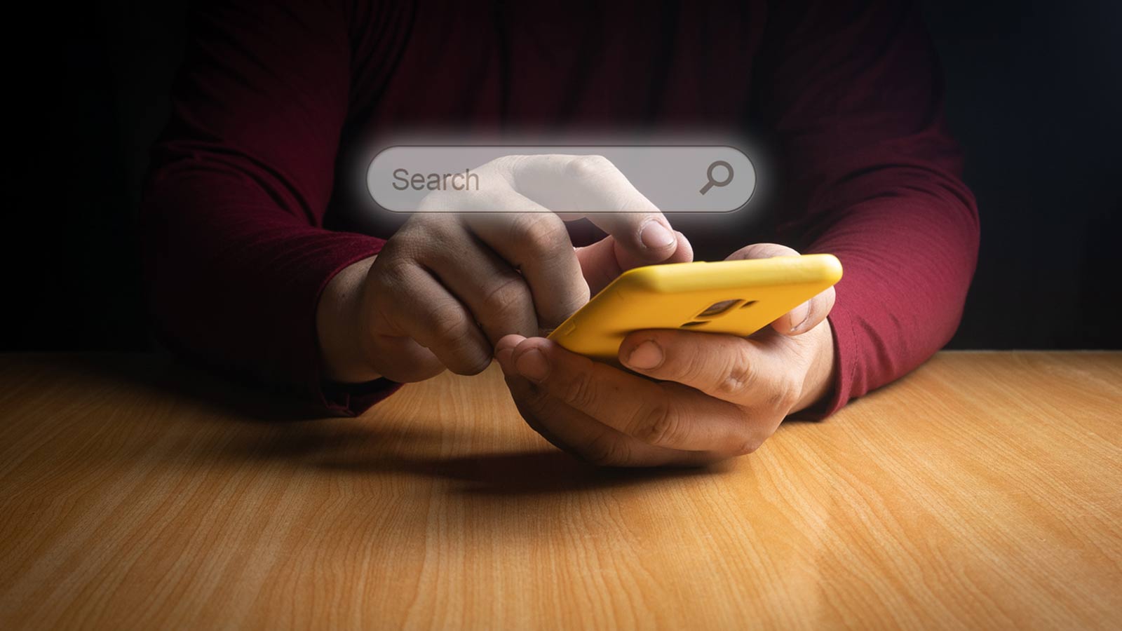 A person in a red shirt is using a yellow smartphone, with a search bar overlay appearing at the top of the image, signifying their focus on an effective SEO strategy.