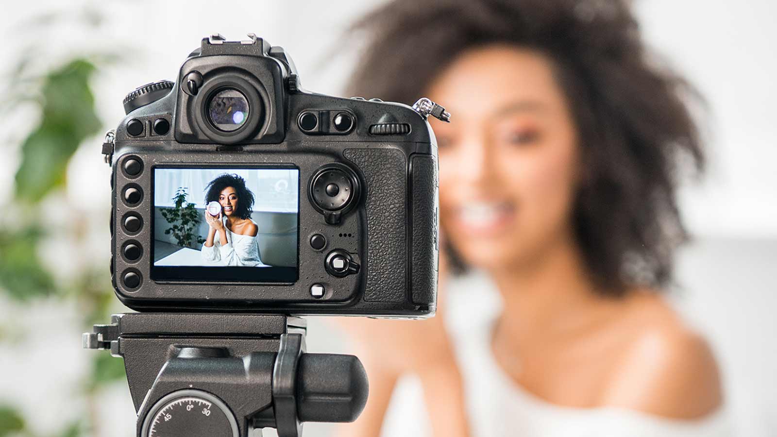 A digital camera on a tripod captures a photo of a smiling person with curly hair, perfectly posed for content creators and influencers seated indoors.