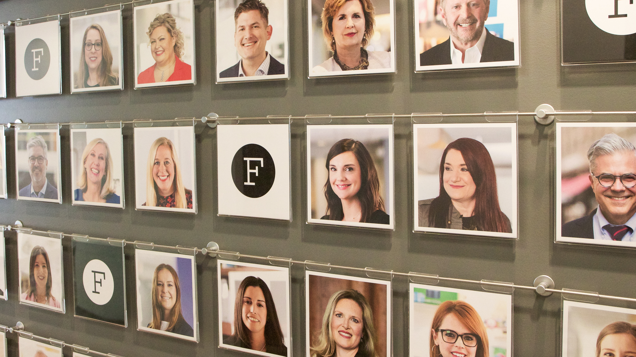 A wall display of headshot photos of various professionals, organized in a grid pattern, with a few photos interspersed with the letter "F" on a black circle background. The inspiring stories behind these faces come to life, reflecting their diverse journeys and achievements.