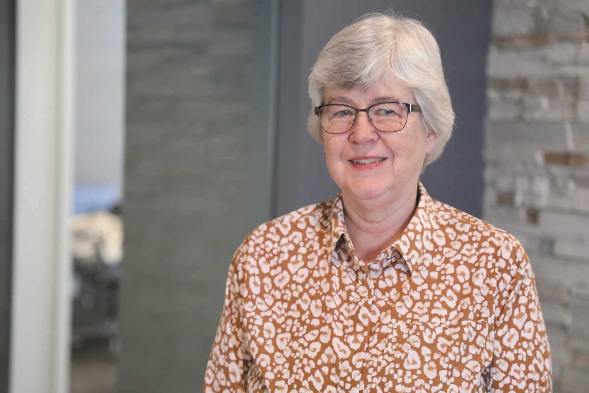 Margaret Reese, a Senior Accounting Specialist at Falls & Co., stands in an indoor setting with short white hair, wearing glasses and a brown patterned shirt