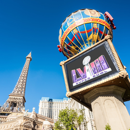 An outdoor sign with a Super Bowl Ad Edition stands in front of a structure resembling the Eiffel Tower in Las Vegas, creating a dynamic visual much like Groundhog Day’s repeated surprises.