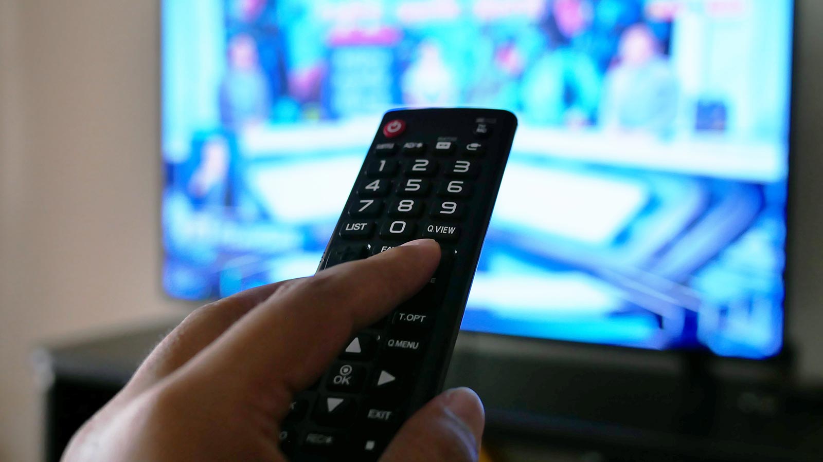 A person points a remote control at a television displaying a colorful, but out-of-focus, screen, showcasing that traditional TV advertising remains effective and relevant in 2022.