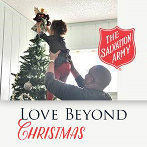 A man lifts a child to place a decoration atop a Christmas tree, celebrating the holidays with warmth and joy. The Salvation Army logo is displayed, with the text reading, "Love Beyond Christmas.