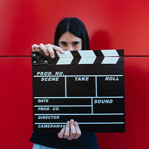 Person holding a clapboard in front of their face against a bright red background, creating an interesting marketing visual.