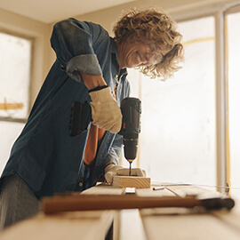 Woman wearing gloves during home improvement project drills a board.