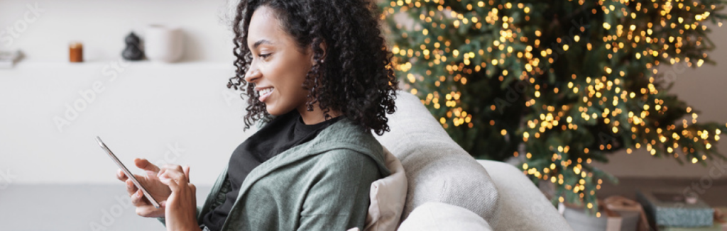 Woman uses her cellphone while sitting in front of a Christmas tree.