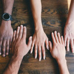 Hands from diverse people lay on a table.