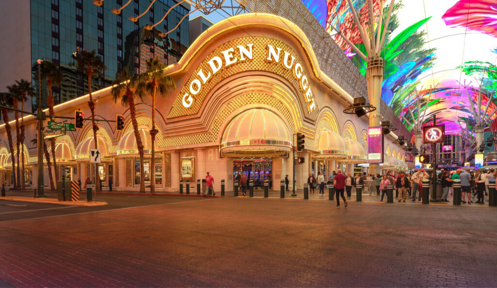 Golden Nugget casino entrance at night with illuminated signs and people standing outside under the lit Fremont Street Experience canopy.